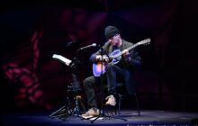 Pochylony mężczyzna w czapce z mocno sfatygowaną gitarą